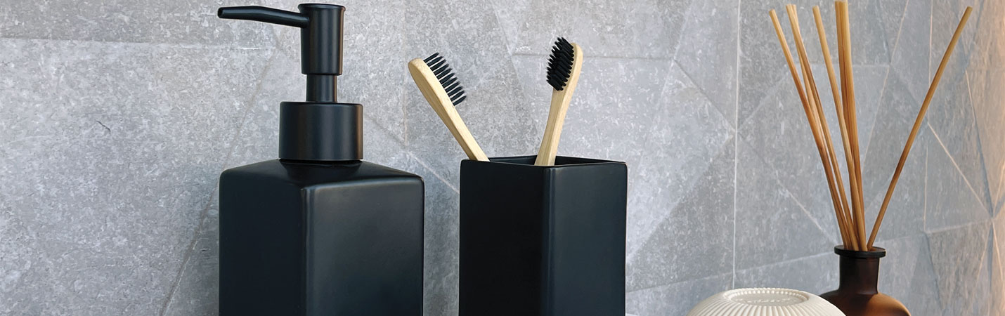 Zahnputzbecher in Schwarz mit Zahnb&uuml;rsten neben Seifenspender und Badaccessoires &ndash; modernes Badaccessoire f&uuml;r Ordnung und Hygiene am Waschtisch